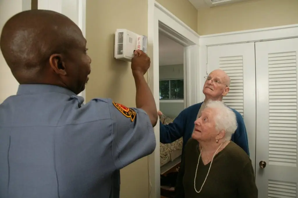 A fire safety officer installs elderly couple a smoke detector in their home
